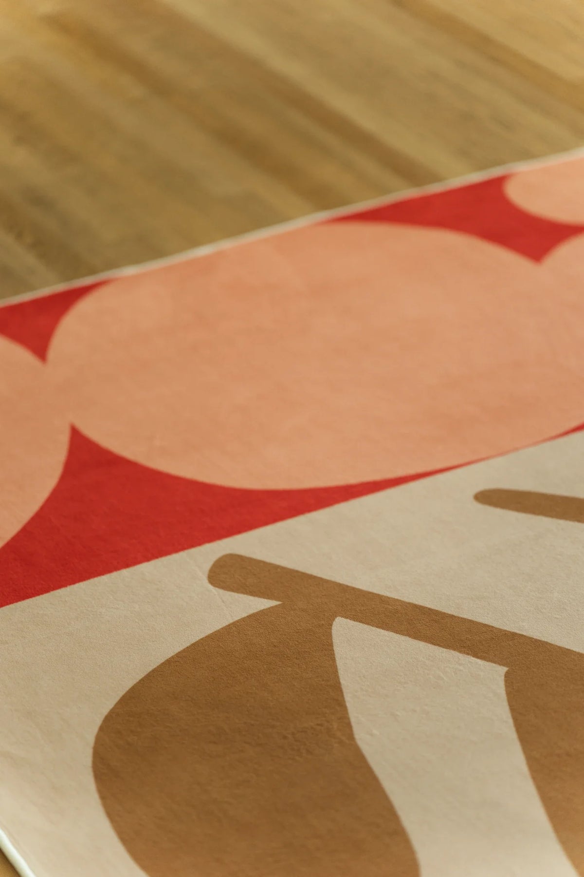 Corner close up on the light wood floor with a pale pink block, tan leaf shape, and red floral edge