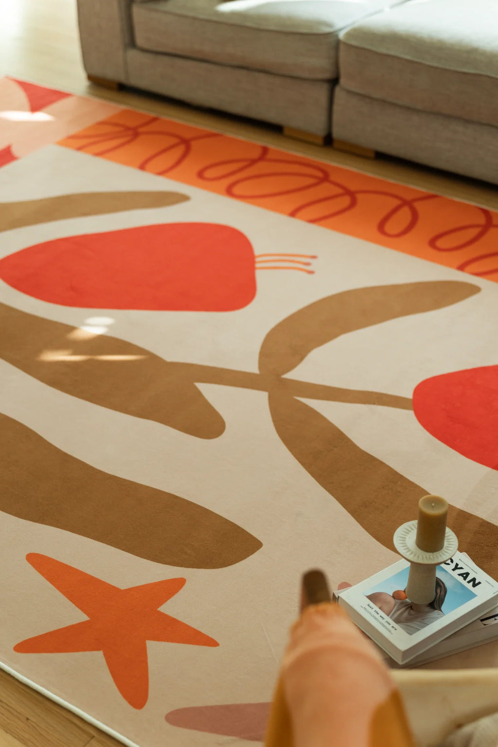 Close up of the abstract floral rug with an orange line border, tan stems, and a small star motif