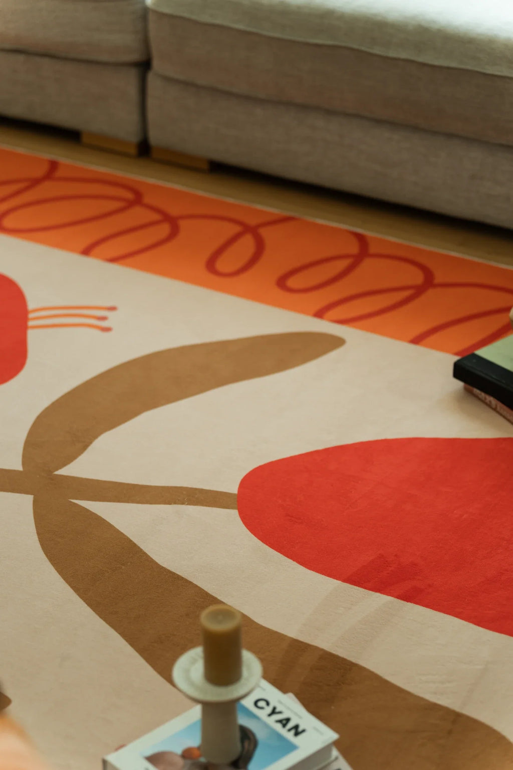 Rug detail beside the sofa with a black book on the surface, showing red blooms and broad tan leaf forms