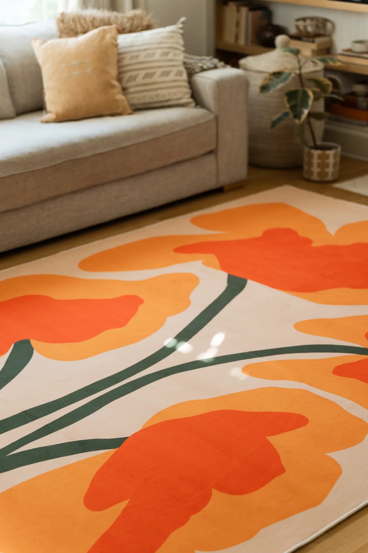 Orange floral sprig rug beside a beige sofa, with layered flower heads and curved stems on a light wood floor