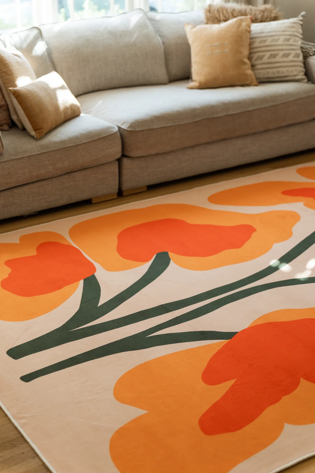 Close crop under a sofa edge showing the floral rug's orange blooms and sweeping dark green stems