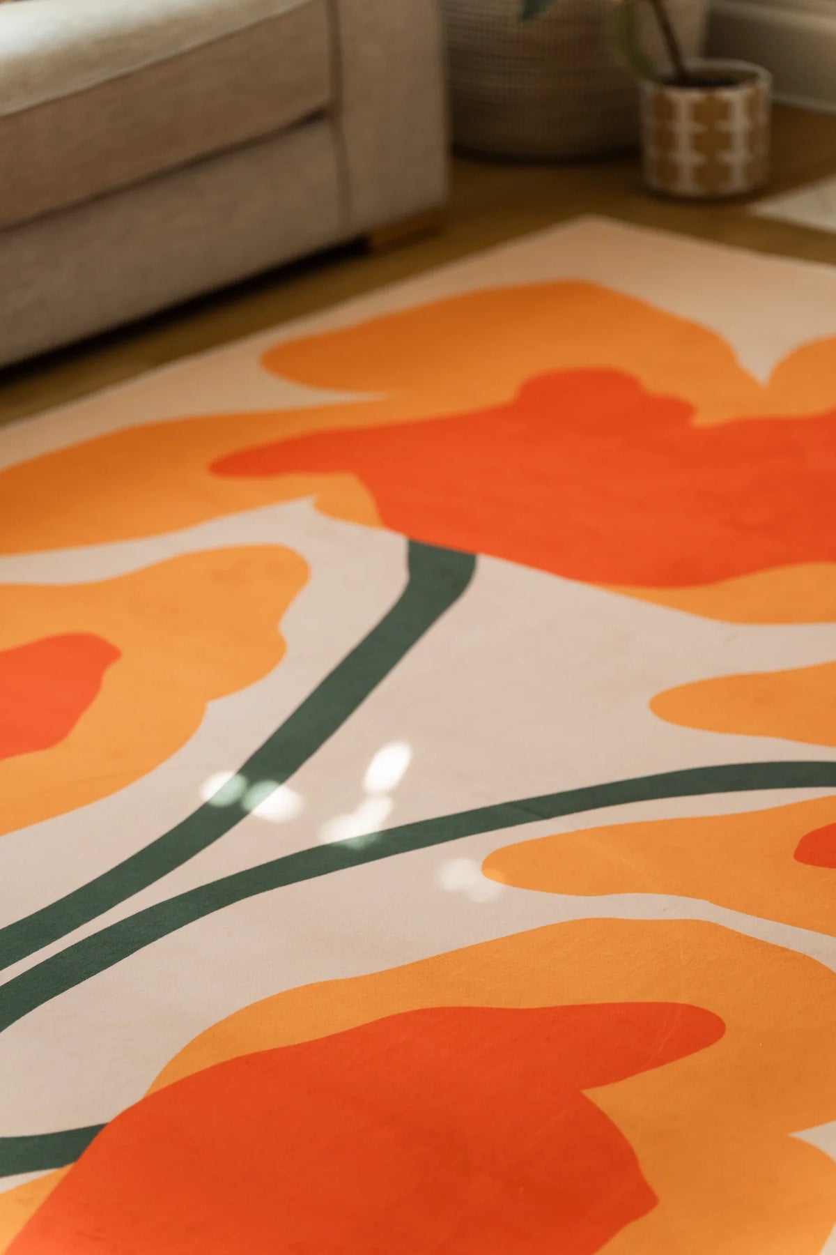 Close view beneath a sofa edge with large orange flower shapes spreading across the cream rug surface