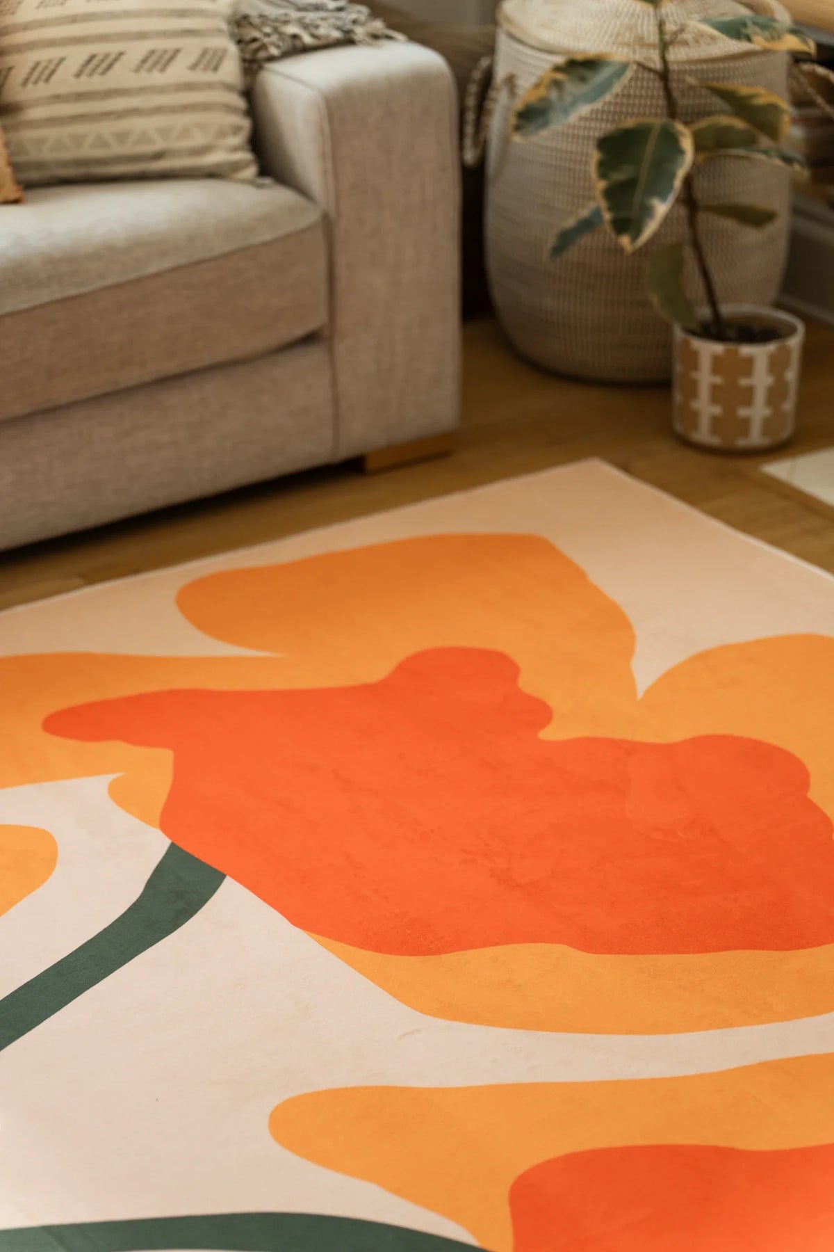 Partial close up of the floral rug beside a sofa and planter, highlighting rounded orange blooms and dark stems