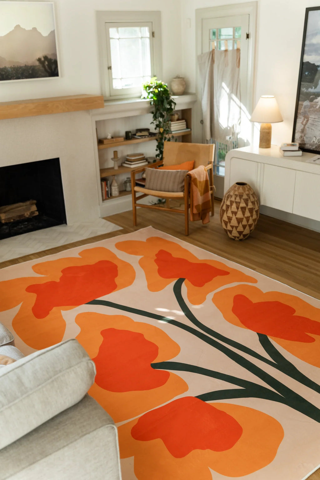 Abstract floral rug in a bright living area beside a sofa and white media console, showing loose orange flower forms