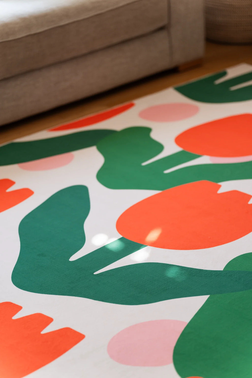 Close up beneath the sofa edge, with orange flower heads and broad green leaves spread across the modern floral area rug