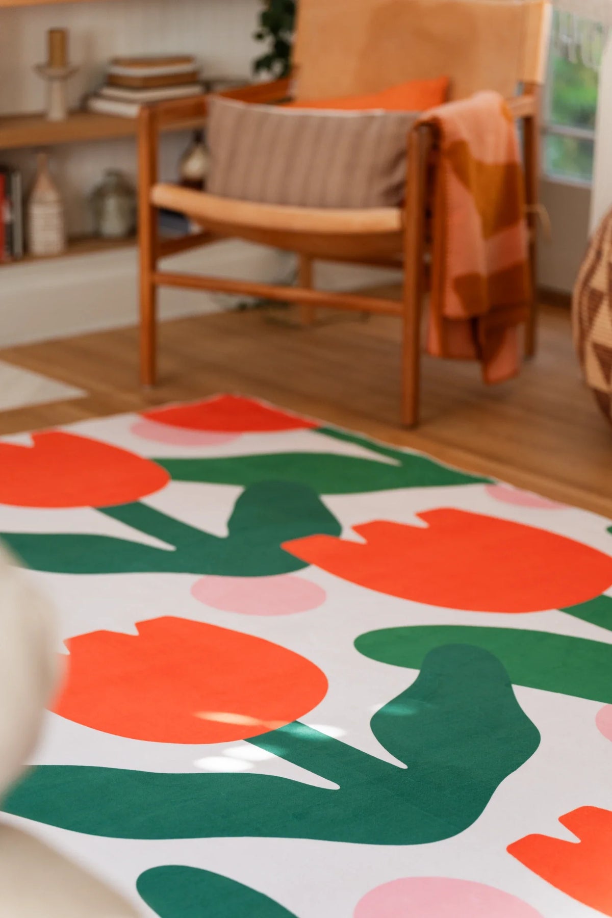 Living room rug detail beside a wood chair, with orange tulip motifs and deep green leaves