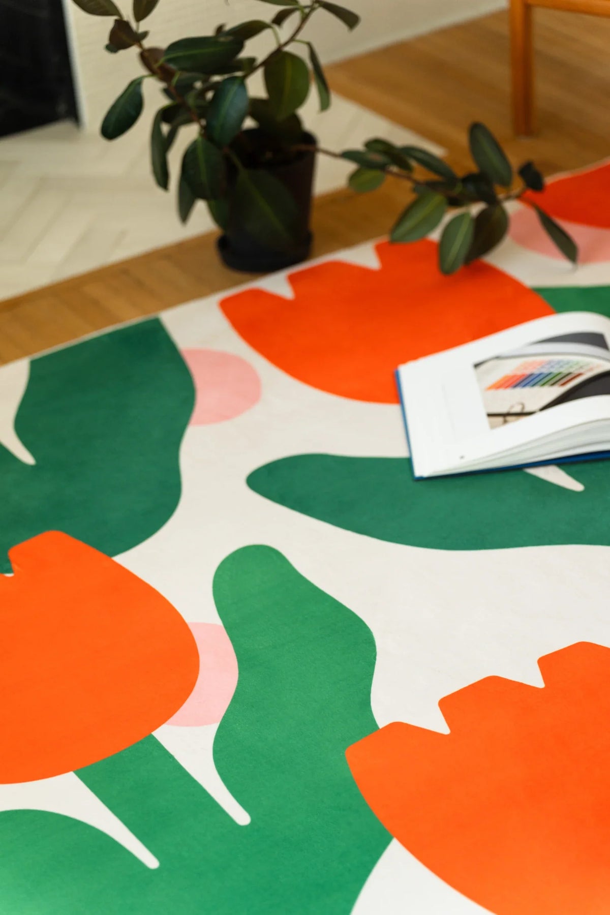 Corner close up with an open book and tray on the rug, highlighting orange petals and bold leaf silhouettes