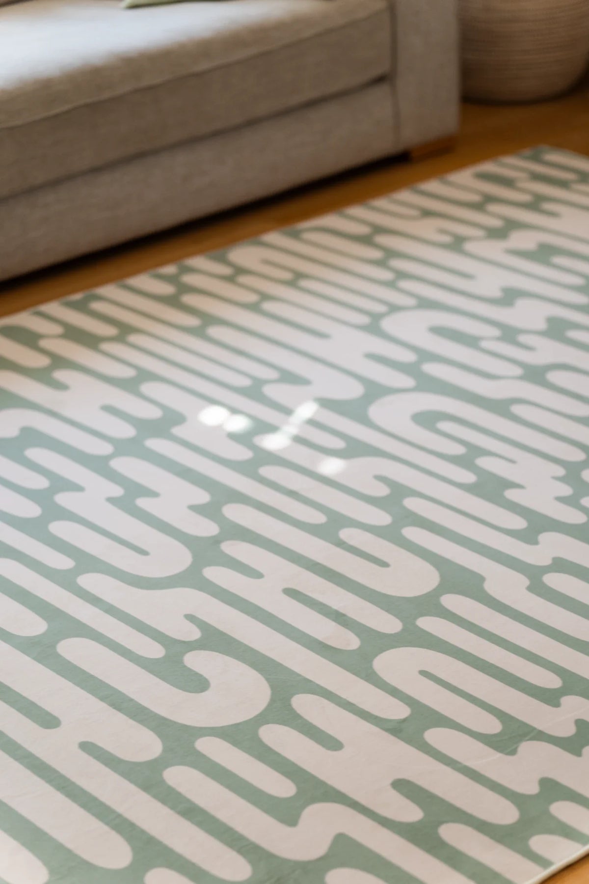 Detail of the wavy area rug with sunlight across the surface, highlighting the flowing green and cream lines