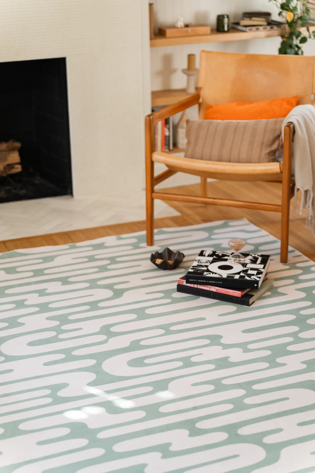 Close up of the green rug beside stacked books and a shell, focused on the curved stripe pattern