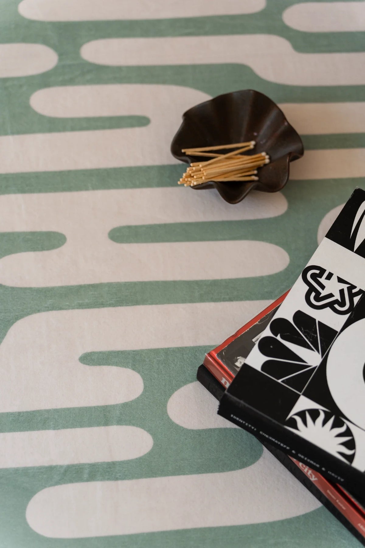 Close up of the green Abstract Wavy Area Rug showing rounded graphic bands beside books and a small decor object