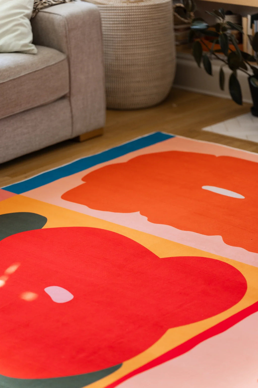 Partial room crop with the rug tucked under the sofa, featuring rounded red petals and a warm yellow ground