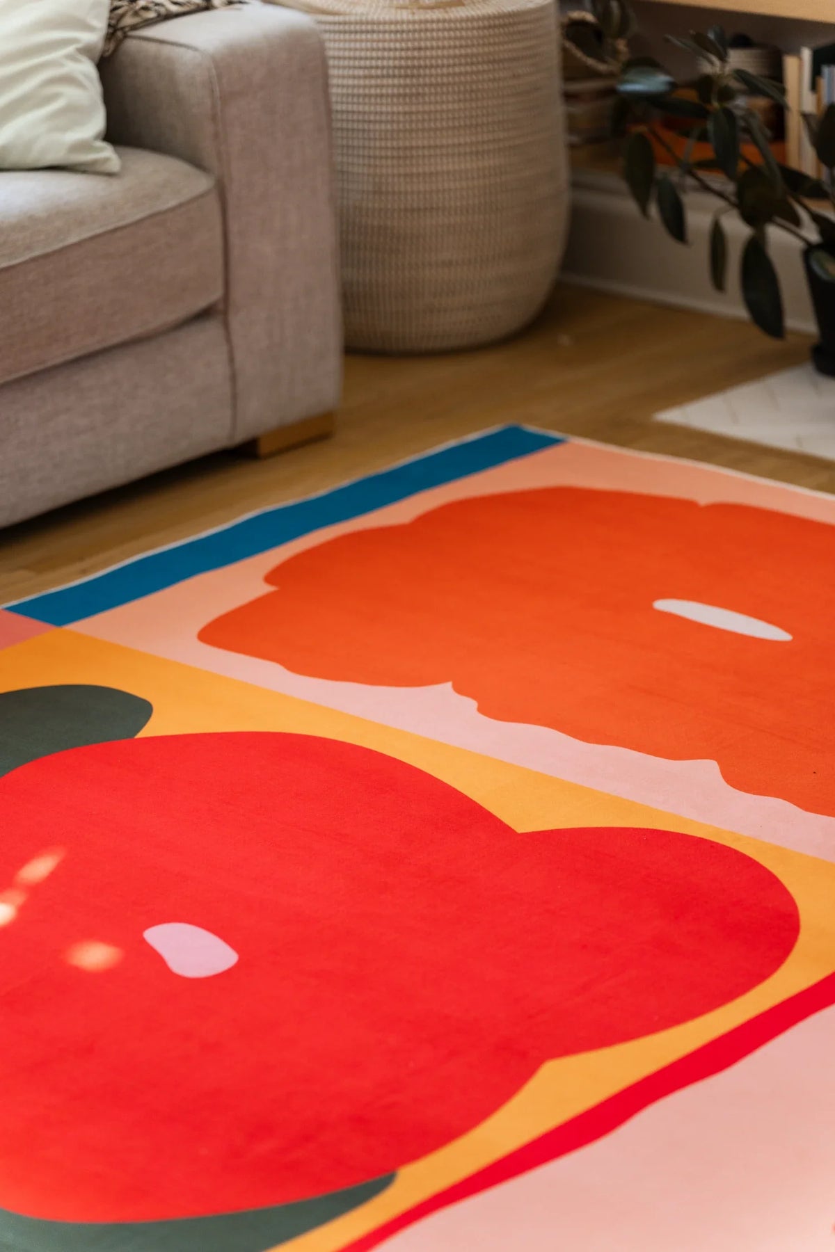 Partial room crop with the rug tucked under the sofa, featuring rounded red petals and a warm yellow ground
