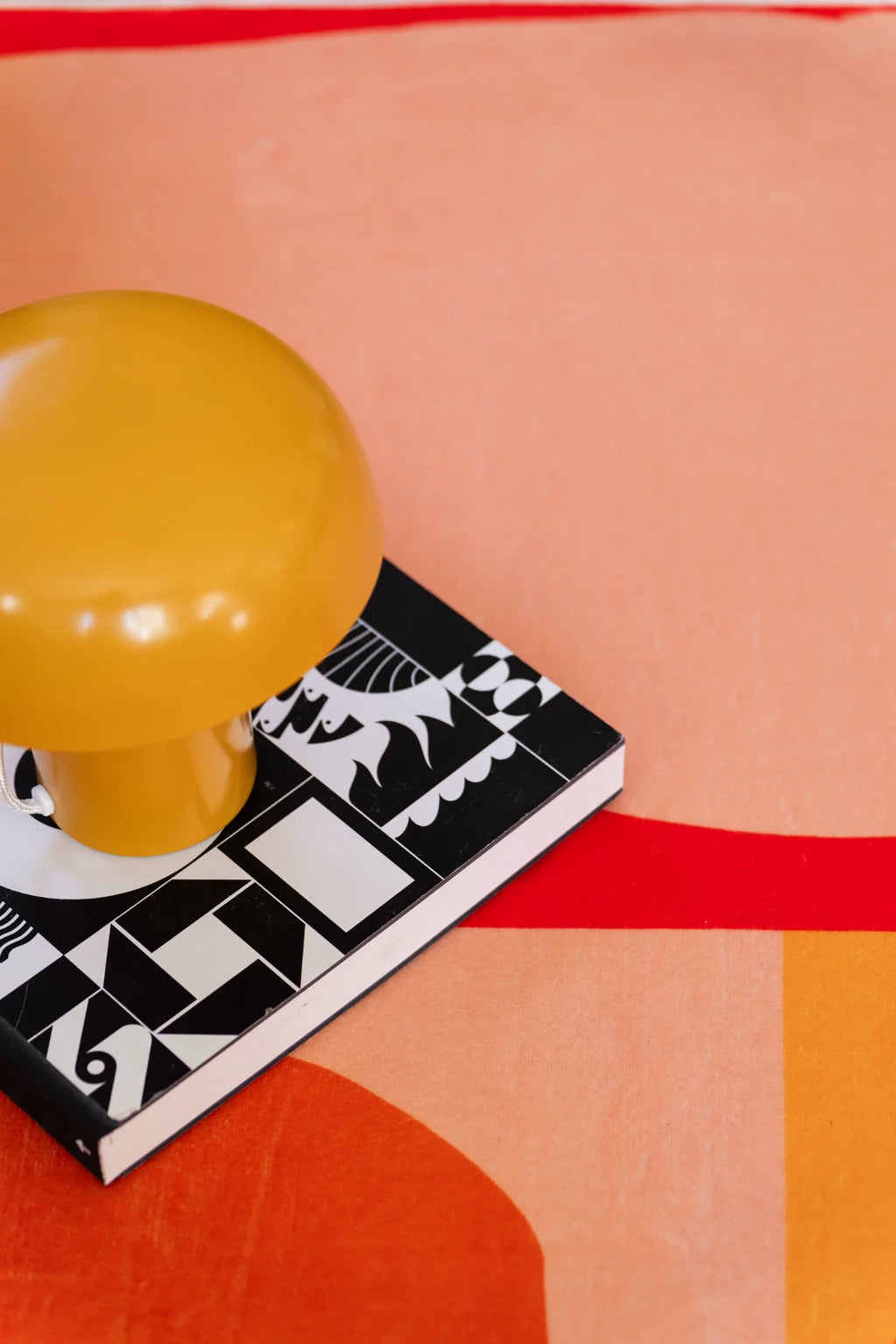 Close up of the multicolor floral rug with a yellow lamp and black book resting on a pink and orange section