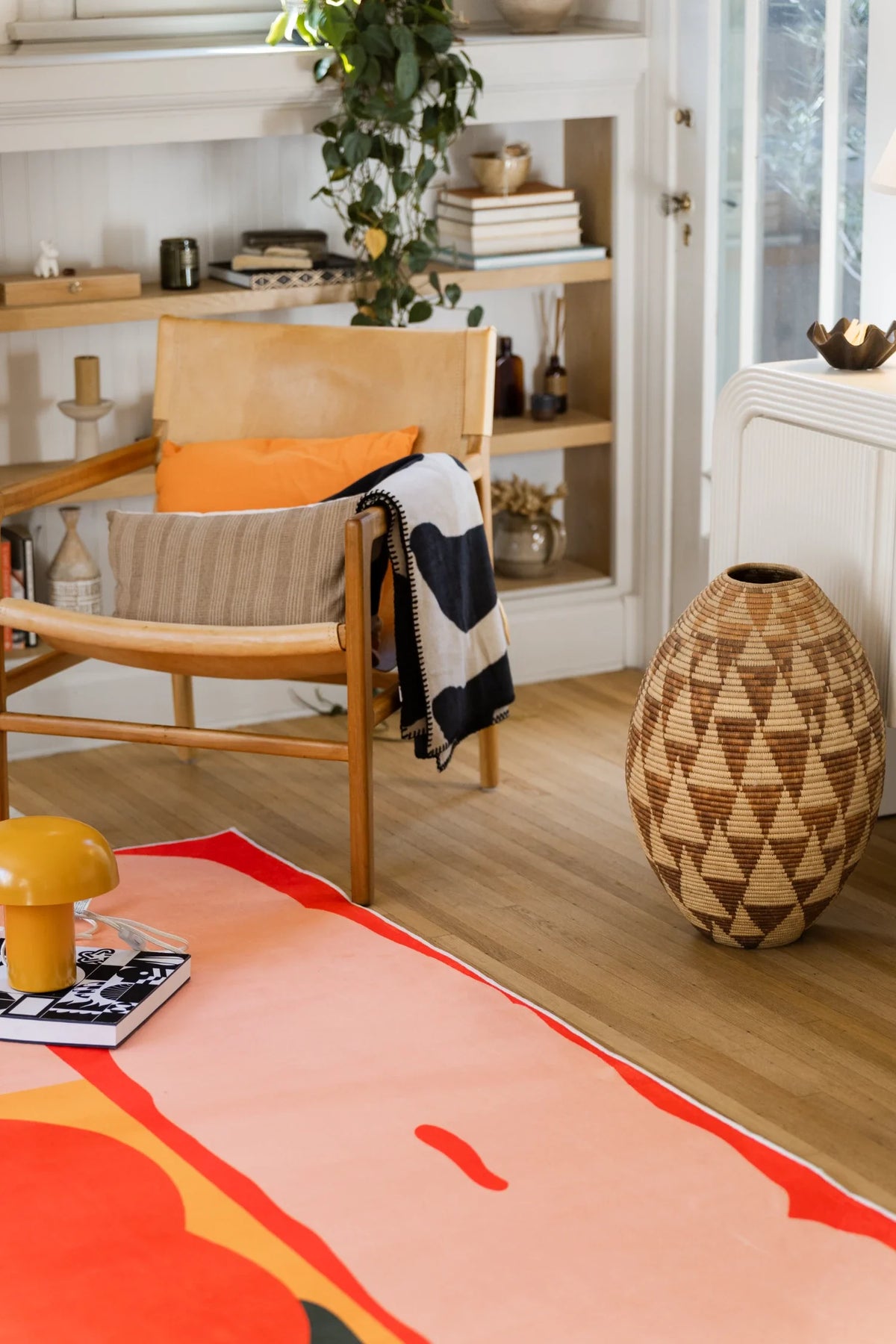 Close view near a wood chair and woven basket, highlighting a pale pink petal panel outlined in red on the rug surface
