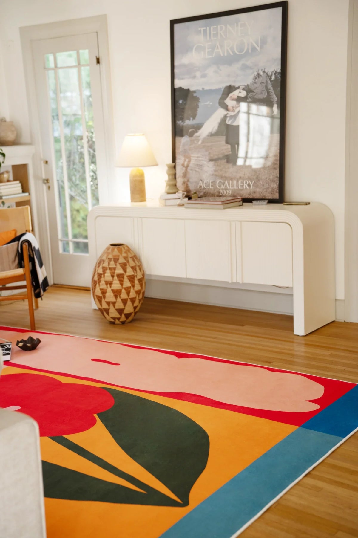Modern flower rug leading toward a white media console and framed art, with a dark green leaf shape and bright blue edge