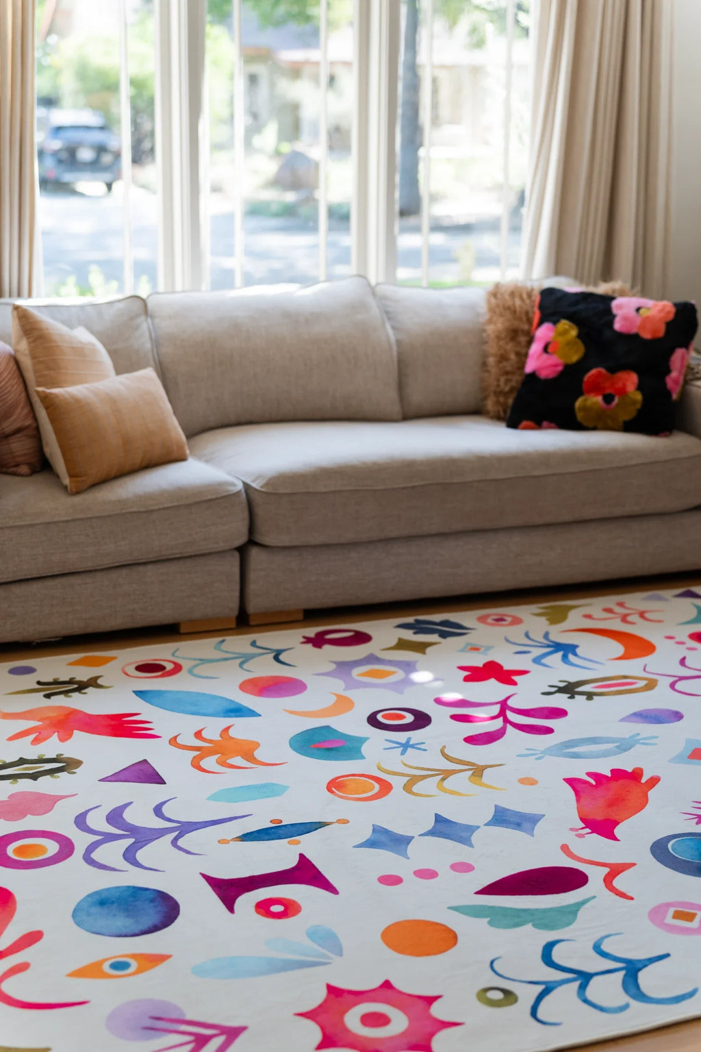 Colorful graphic rug tucked beside a beige sofa in a bright living room, with playful all over symbols across the surface