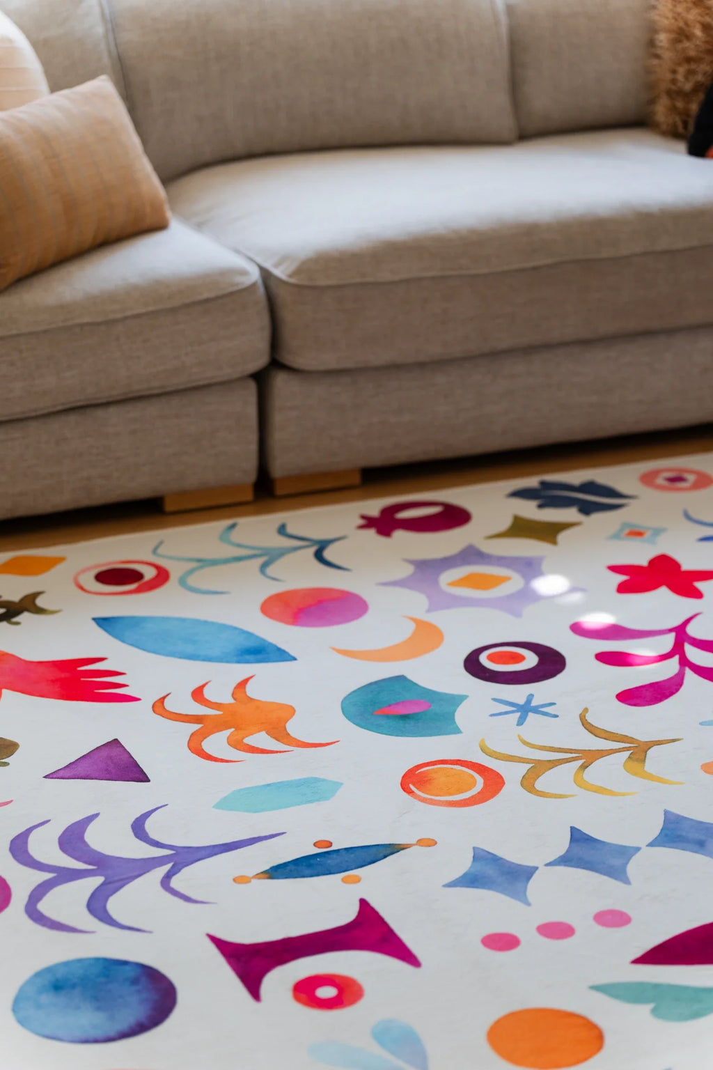 Close crop under the sofa edge, highlighting the rug's dense pattern of stars, petals, circles, and curved graphic motifs