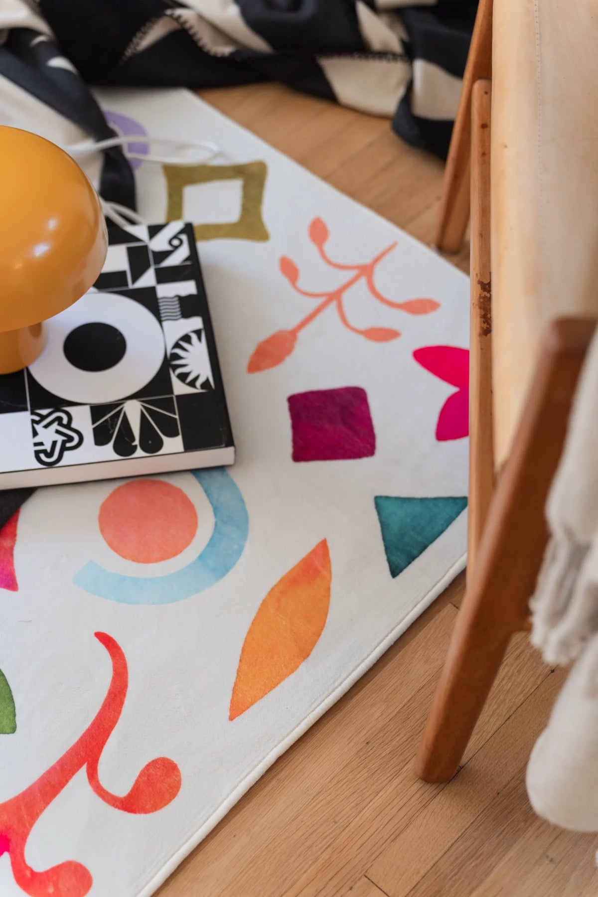 Close detail of the rug under a chair leg, with orange, pink, blue, and green symbols arranged in an all over pattern