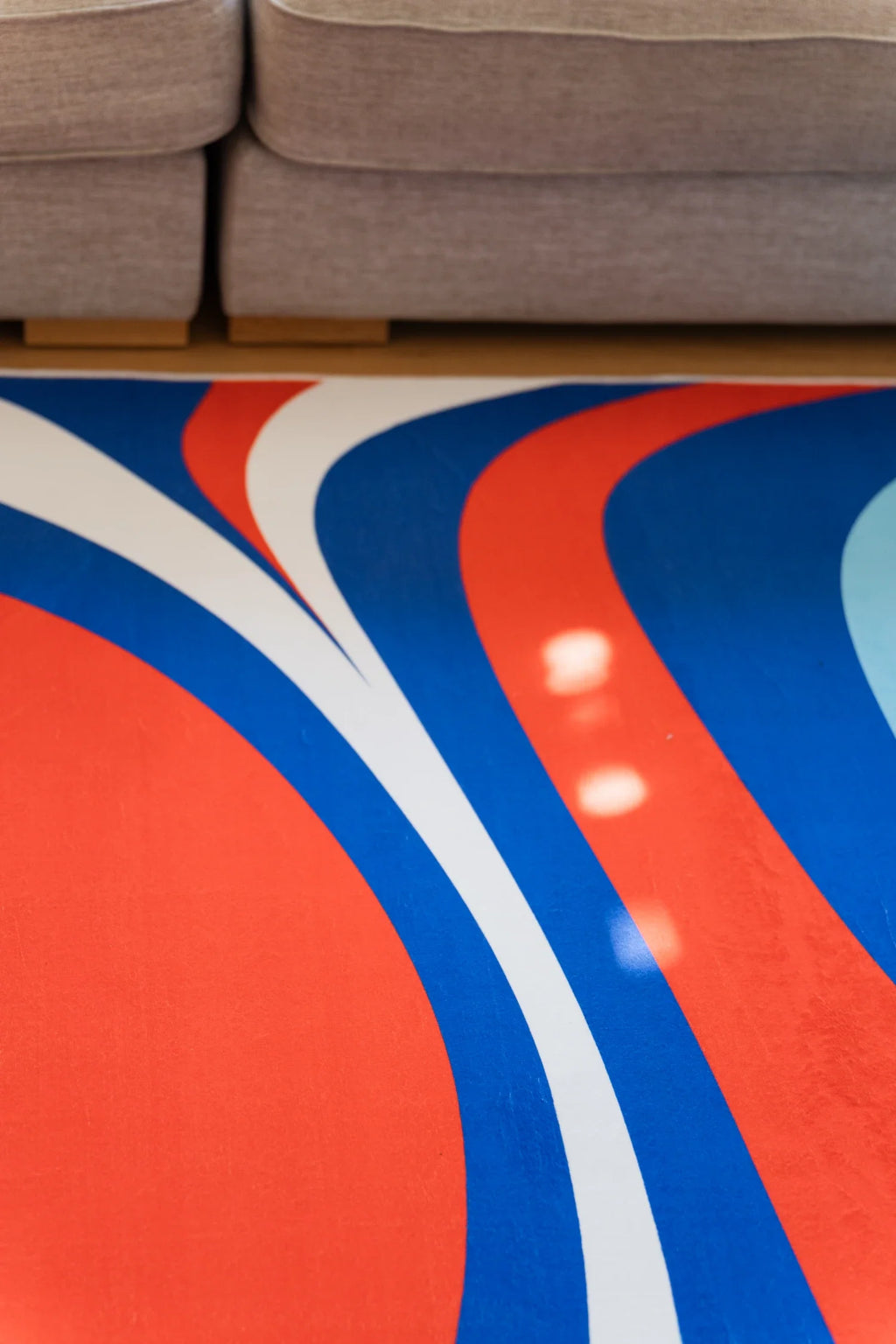Close up of the blue and red rug beneath a gray sofa, showing bold royal blue and red organic curves