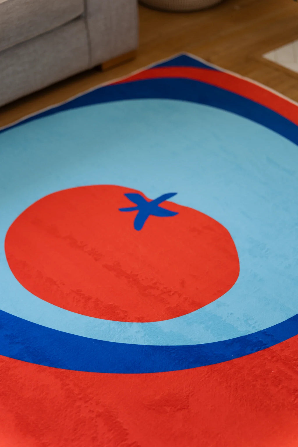 Close up of the blue and red rug with a pale blue circle, red tomato center, and small blue stem