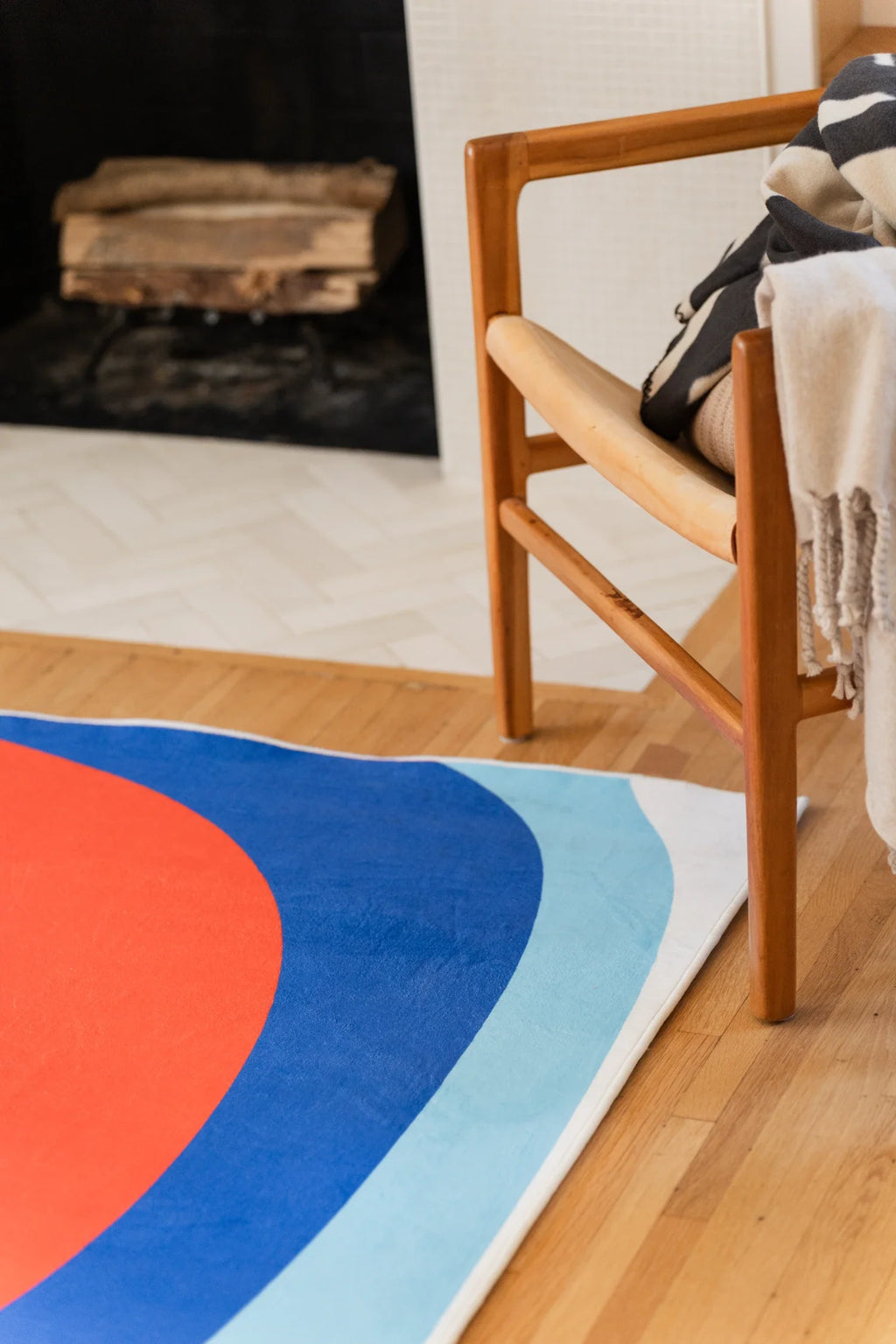Partial view of the blue and red rug beside a wood chair, showing broad red, royal blue, and pale blue arcs