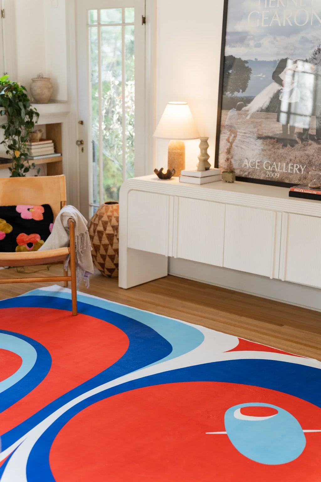Blue and red abstract rug in a modern living room with a white media console, lamp, and framed artwork