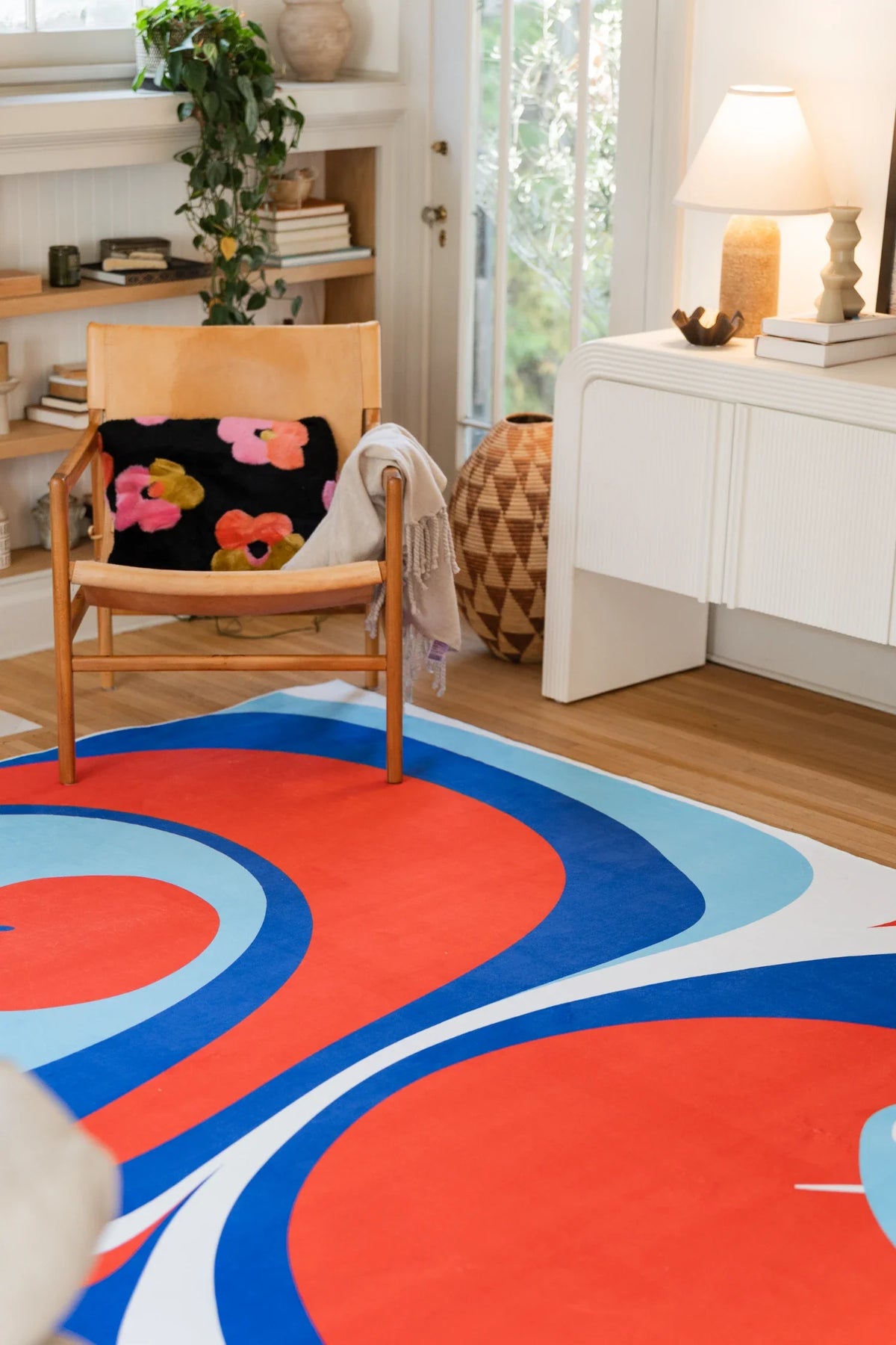Tomato Twist rug in blue and red in a bright room with a wood chair, white cabinet, and floral pillow