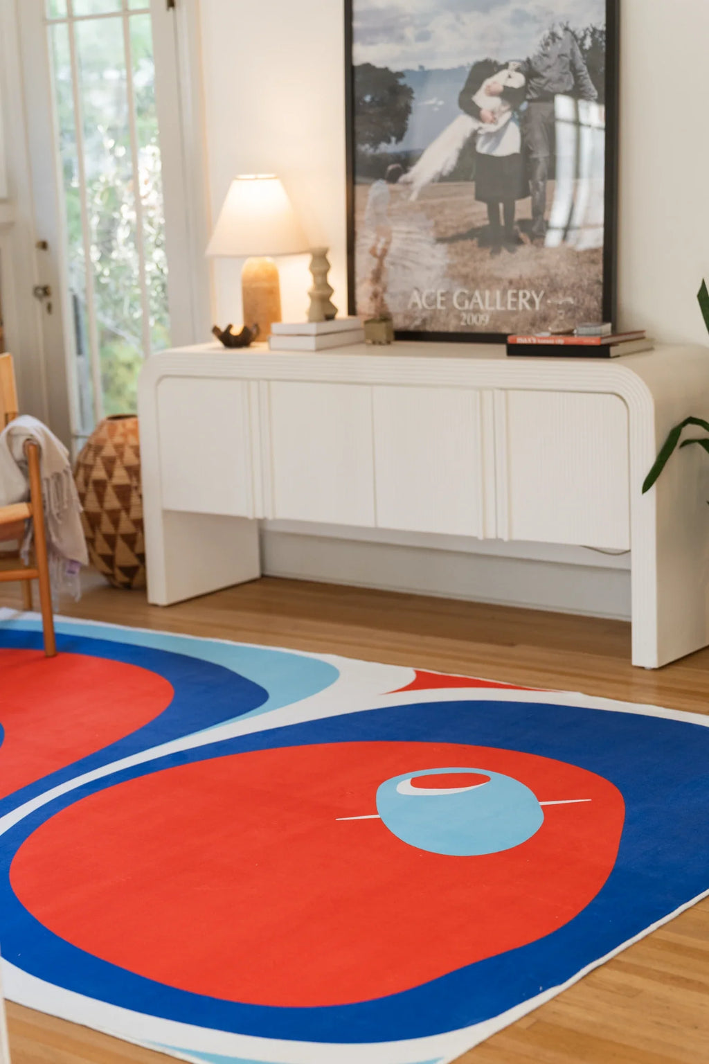Blue and red rug in a bright corner with a white media console and framed art, showing rounded tomato shapes