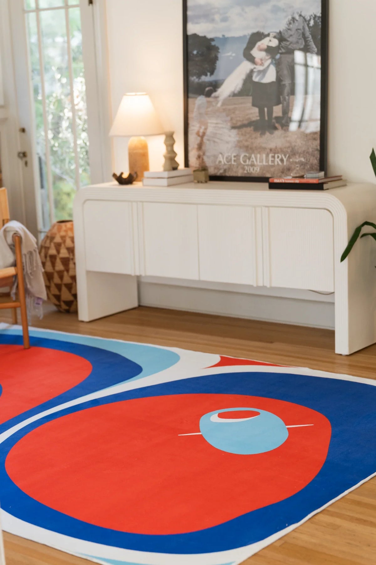 Blue and red rug in a bright corner with a white media console and framed art, showing rounded tomato shapes