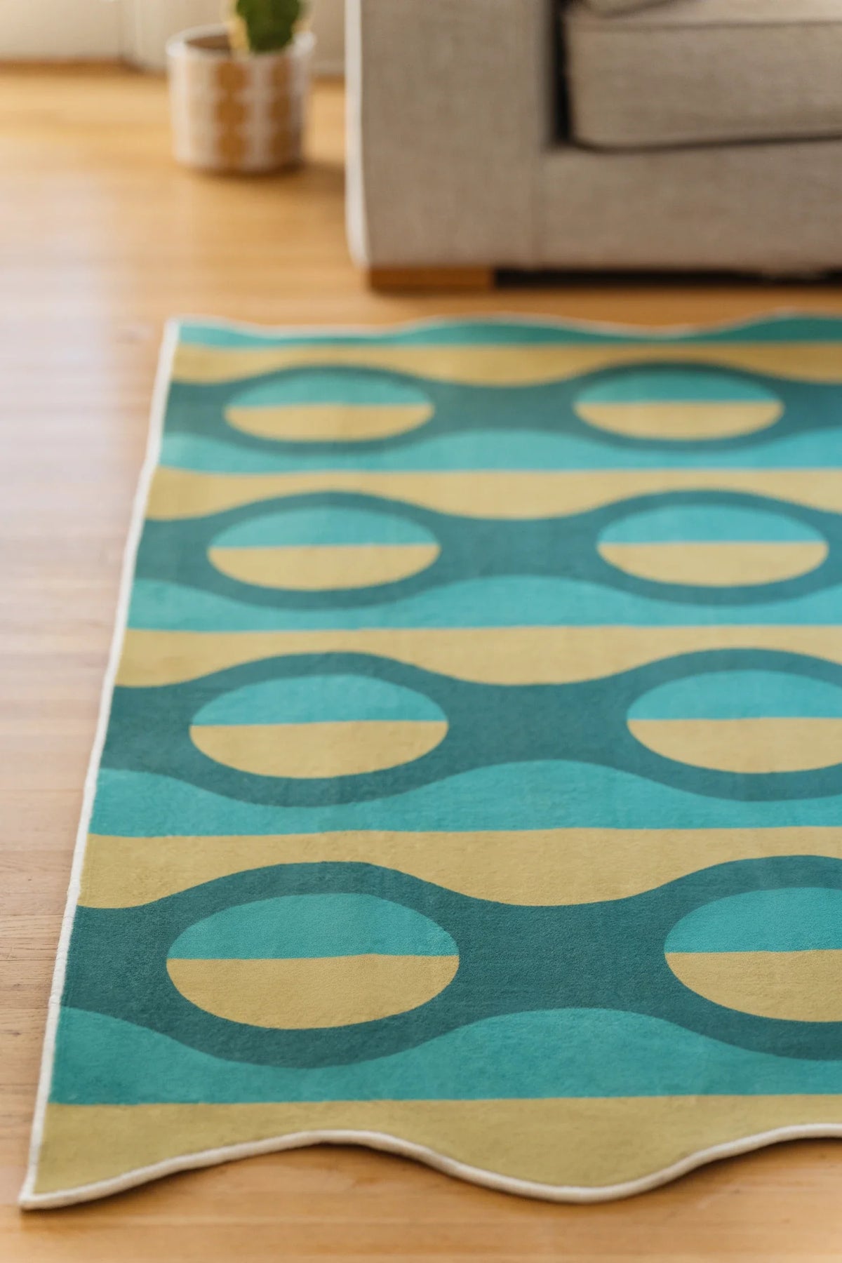 Geometric area rug cropped at the far end, showing teal stripes, mustard ovals, and a softly wavy edge