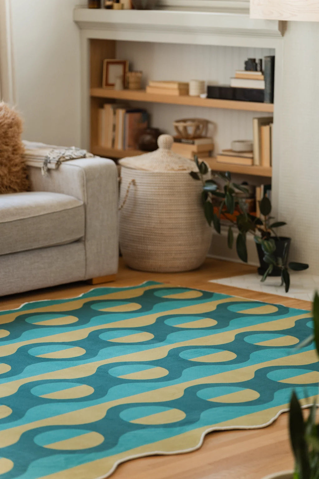 Modern striped area rug beside a beige sofa and open shelving, showing teal bands and mustard oval repeats