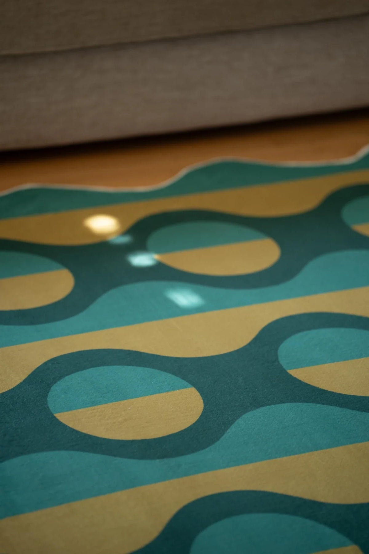 Green geometric rug under the sofa edge, showing mustard ovals repeated across deep teal vertical bands