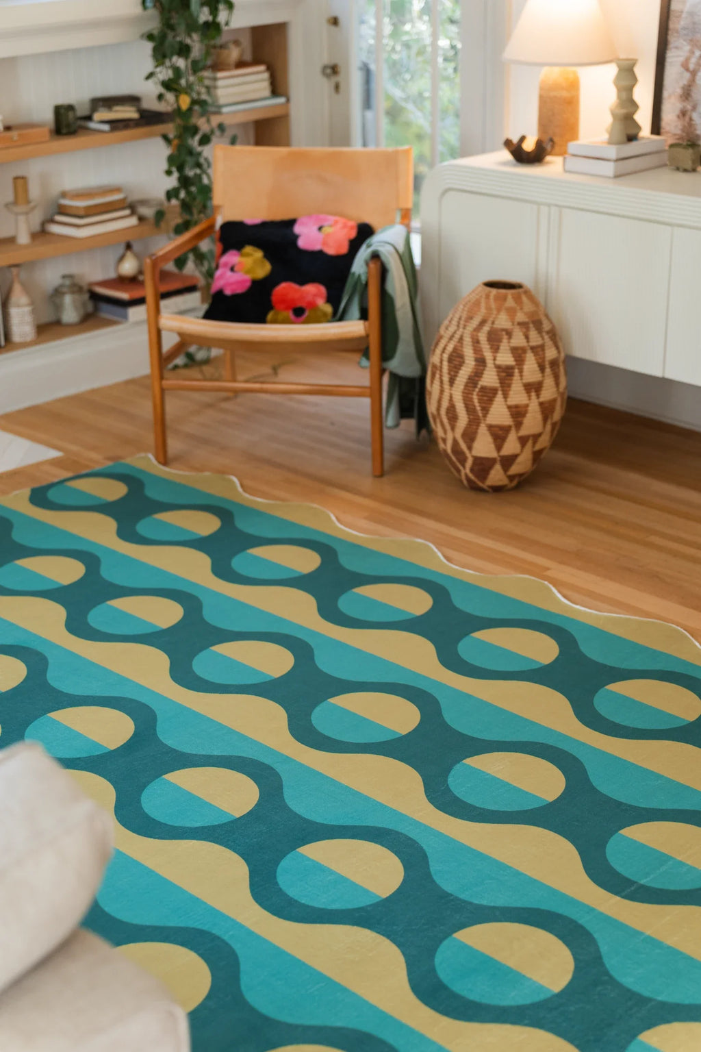 Green geometric rug near a white media console and orange chair, with graphic stripes on a light wood floor