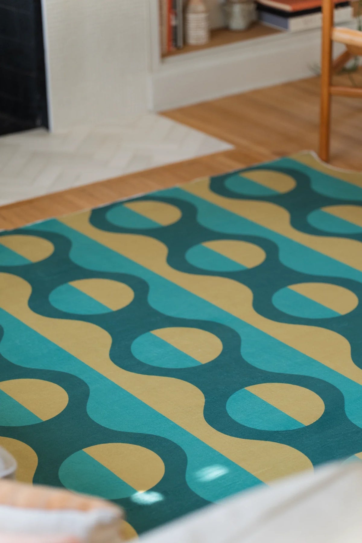 Green and mustard striped rug near the fireplace, with curved vertical bands extending toward a wood chair