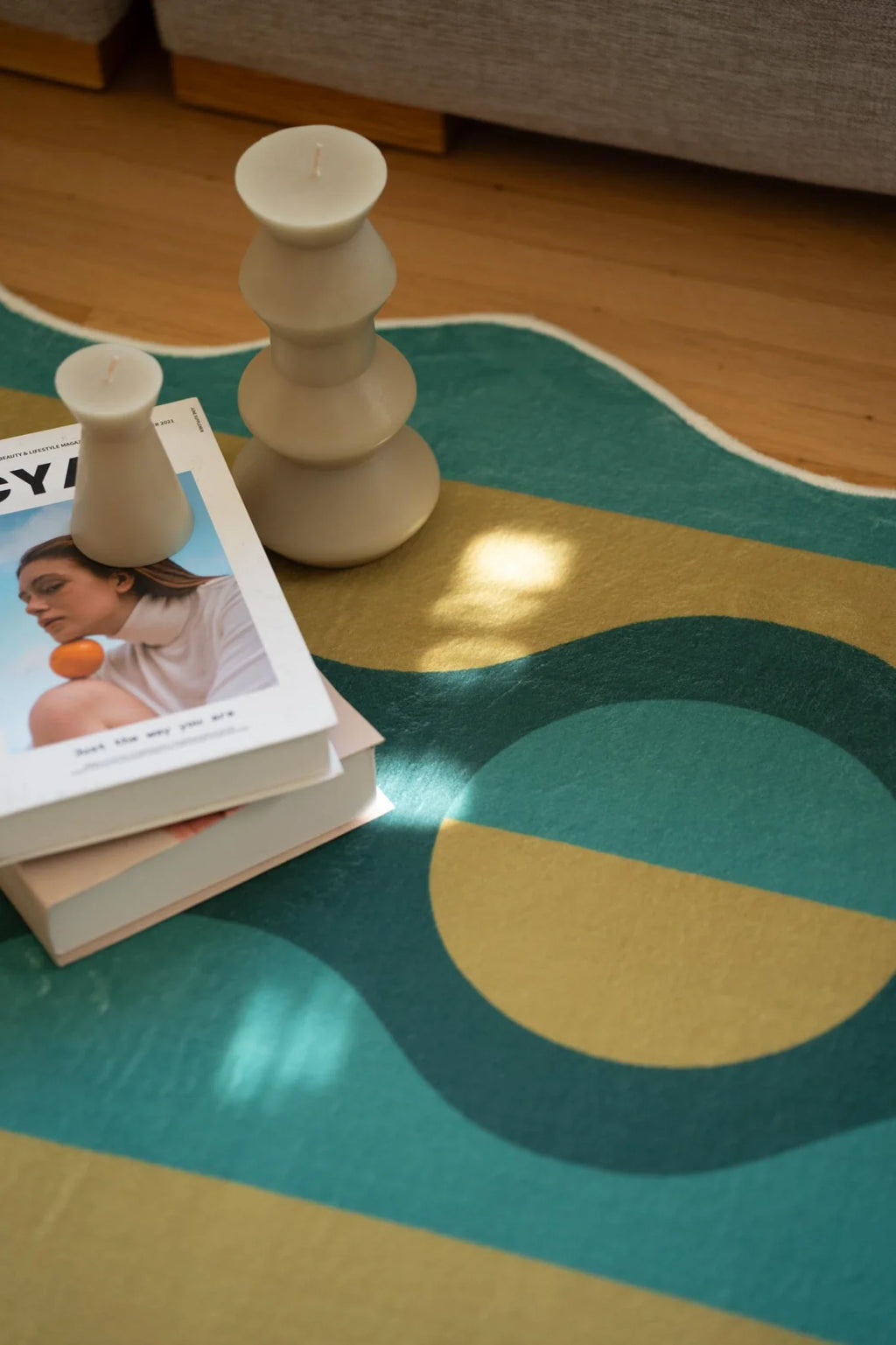 Close up of the green striped rug with stacked books and a wood toy on the surface beside the sofa
