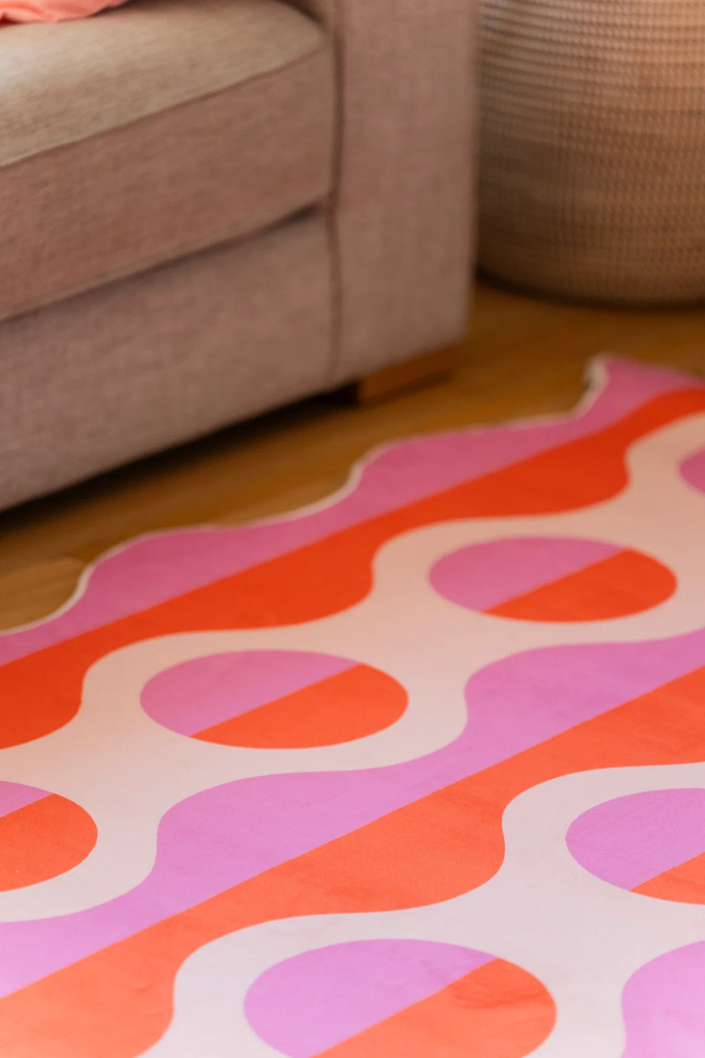 Partial crop under the sofa showing the geometric striped rug with coral bands and pale pink oval repeats