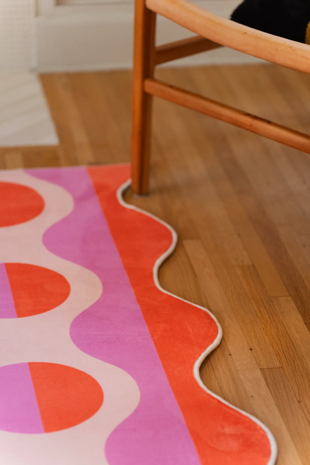 Pink striped area rug beside a wood chair leg, with rounded orange motifs and an irregular wavy border