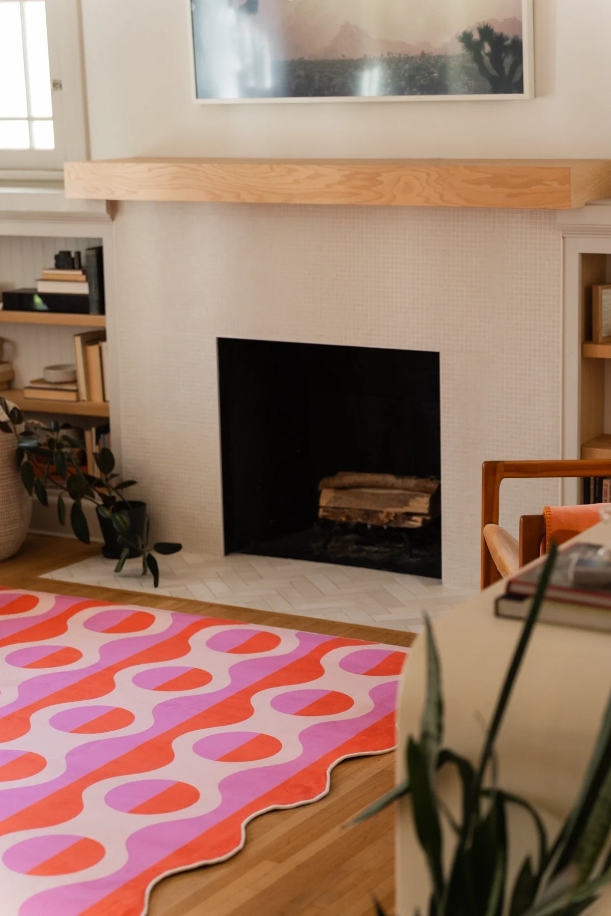 Striped area rug near the fireplace and plant, with pink ground, orange ovals, and warm coral bands