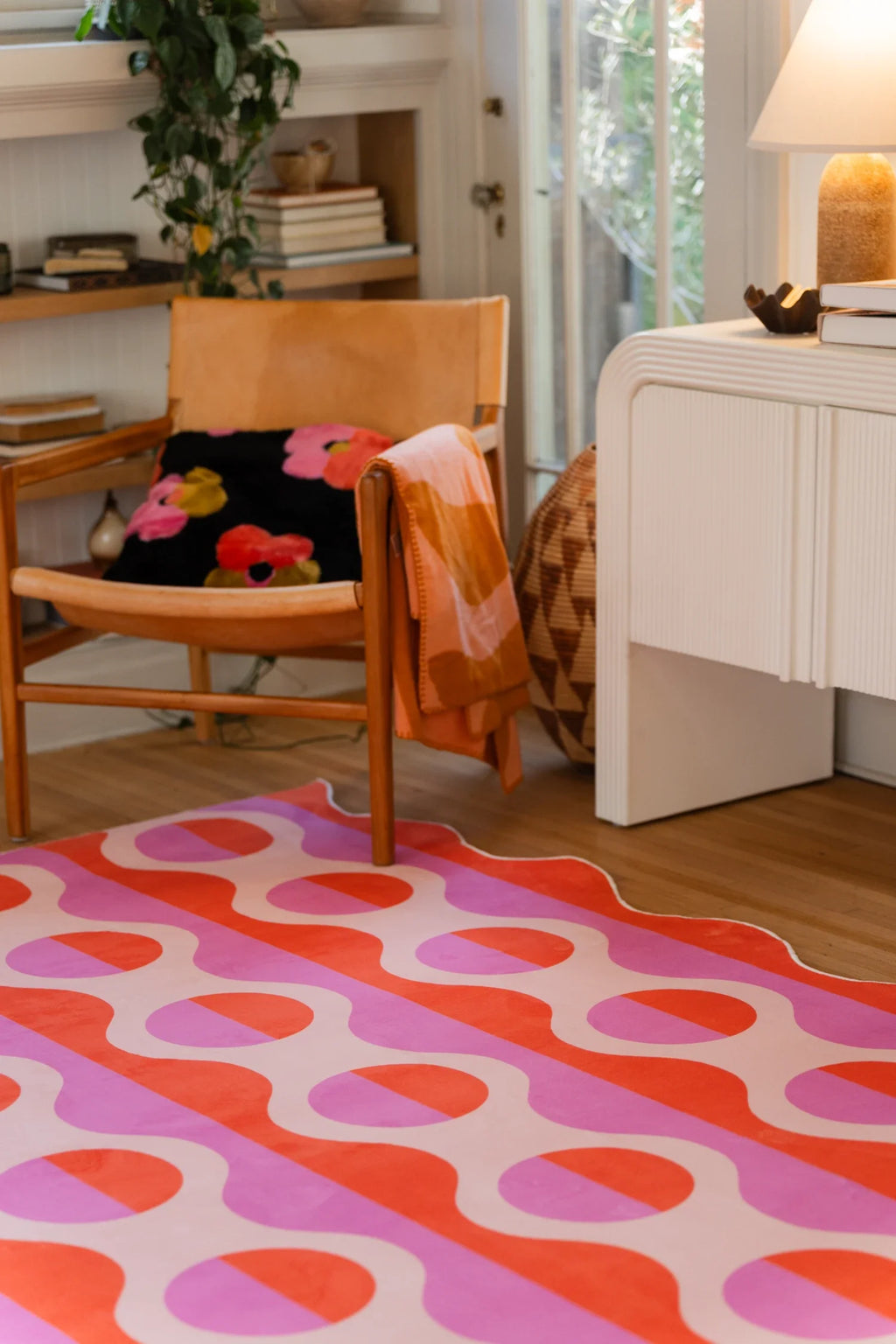 Retro geometric rug near a white media console and orange chair, with pink and orange stripes across the floor