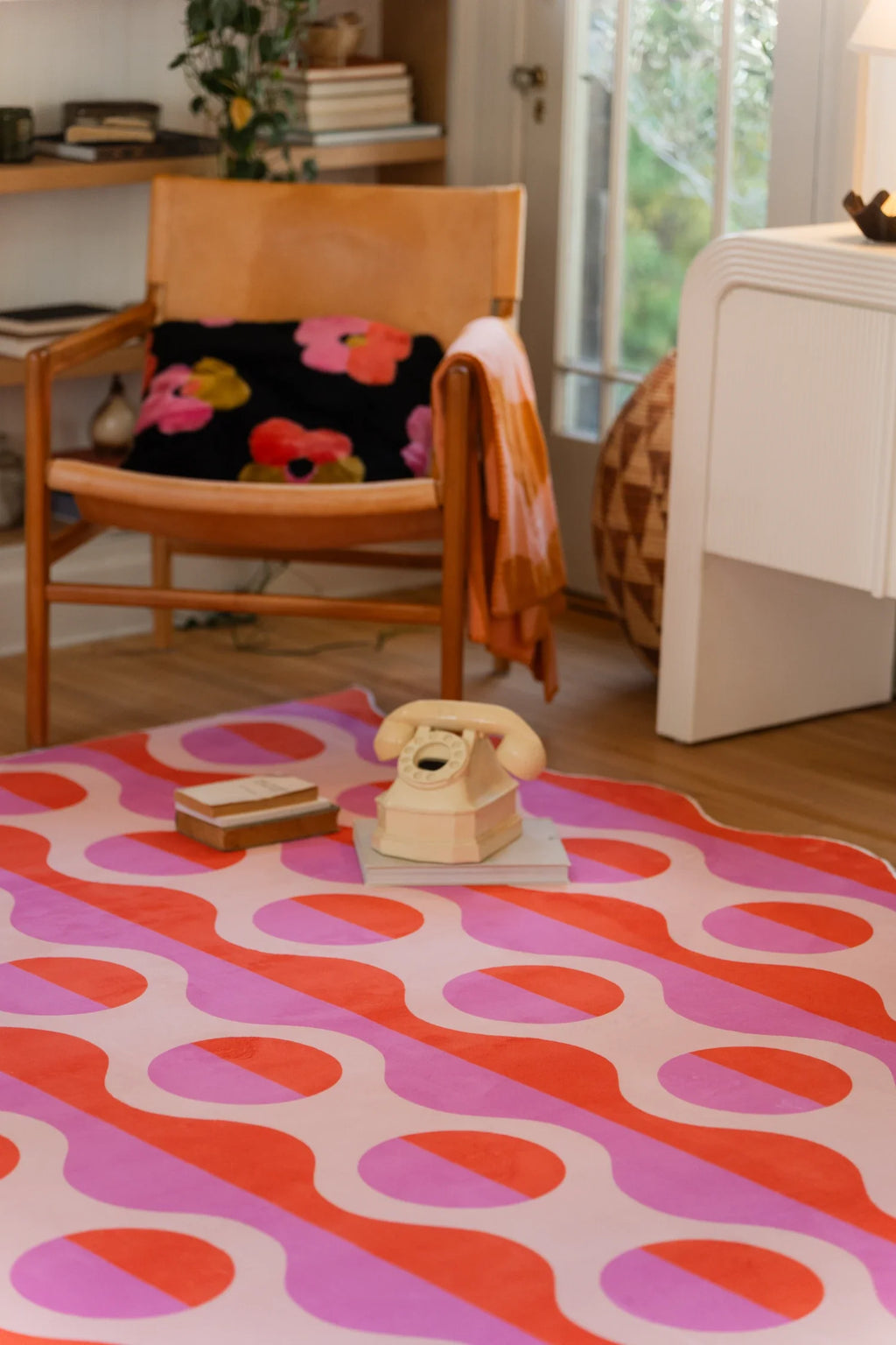 Pink and orange striped rug beside a chair and mugs, showing rounded oval motifs and flowing vertical bands