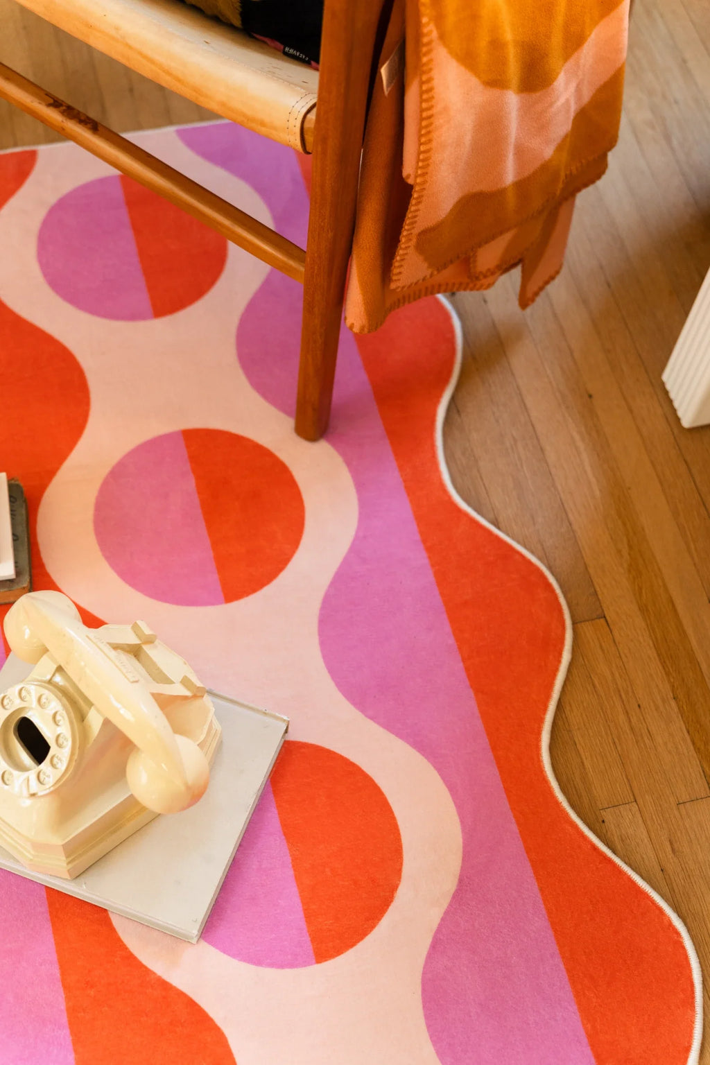 Close detail of the striped rug beside a chair leg and books, showing pink bands, orange ovals, and a wavy edge