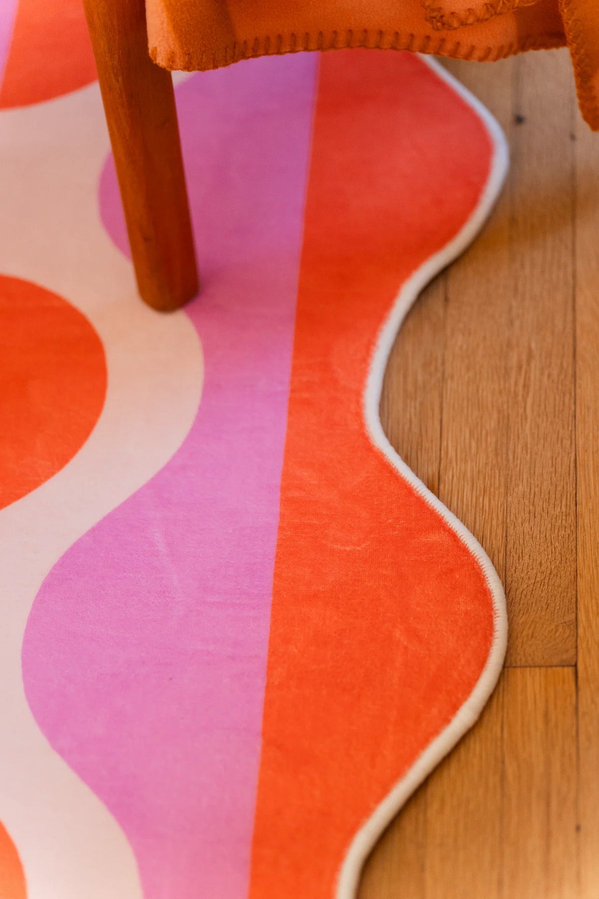 Edge close up of the pink and orange rug, focused on the scalloped border and bold striped color blocks