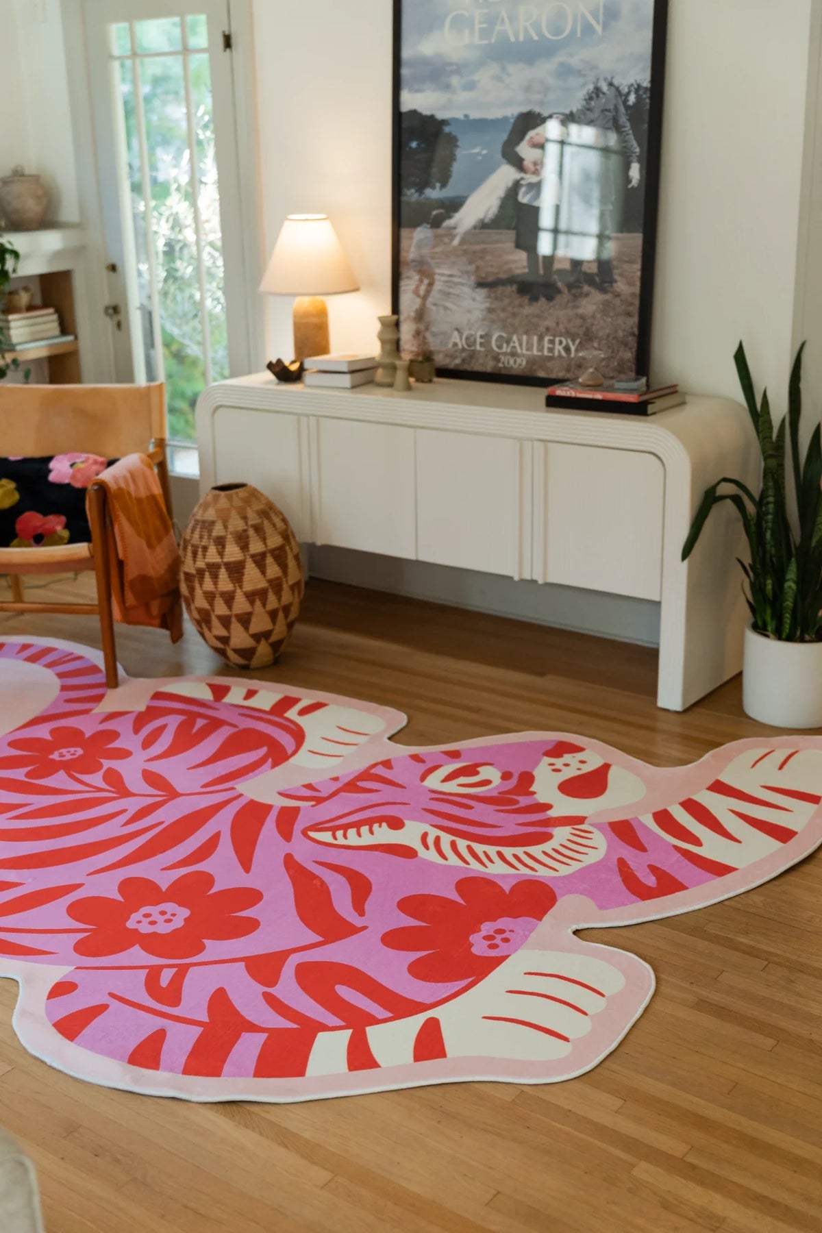 Wide corner view of the bold tiger shaped rug near a media console, lamp, and plant on a clean wood floor