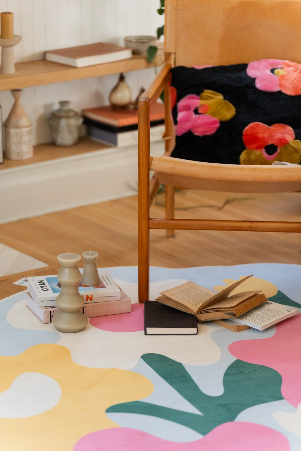 Close view near a wood chair and books, highlighting the colorful flower rug with pink petals, yellow blooms, and white flowers