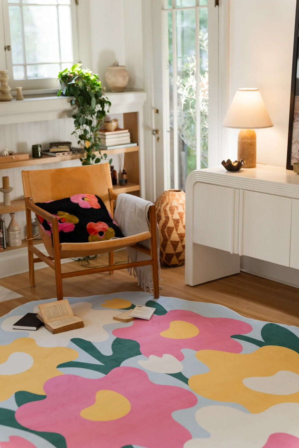 Colorful flower rug near a white media console and lamp, with oversized blossoms spread across an irregular pale blue shape