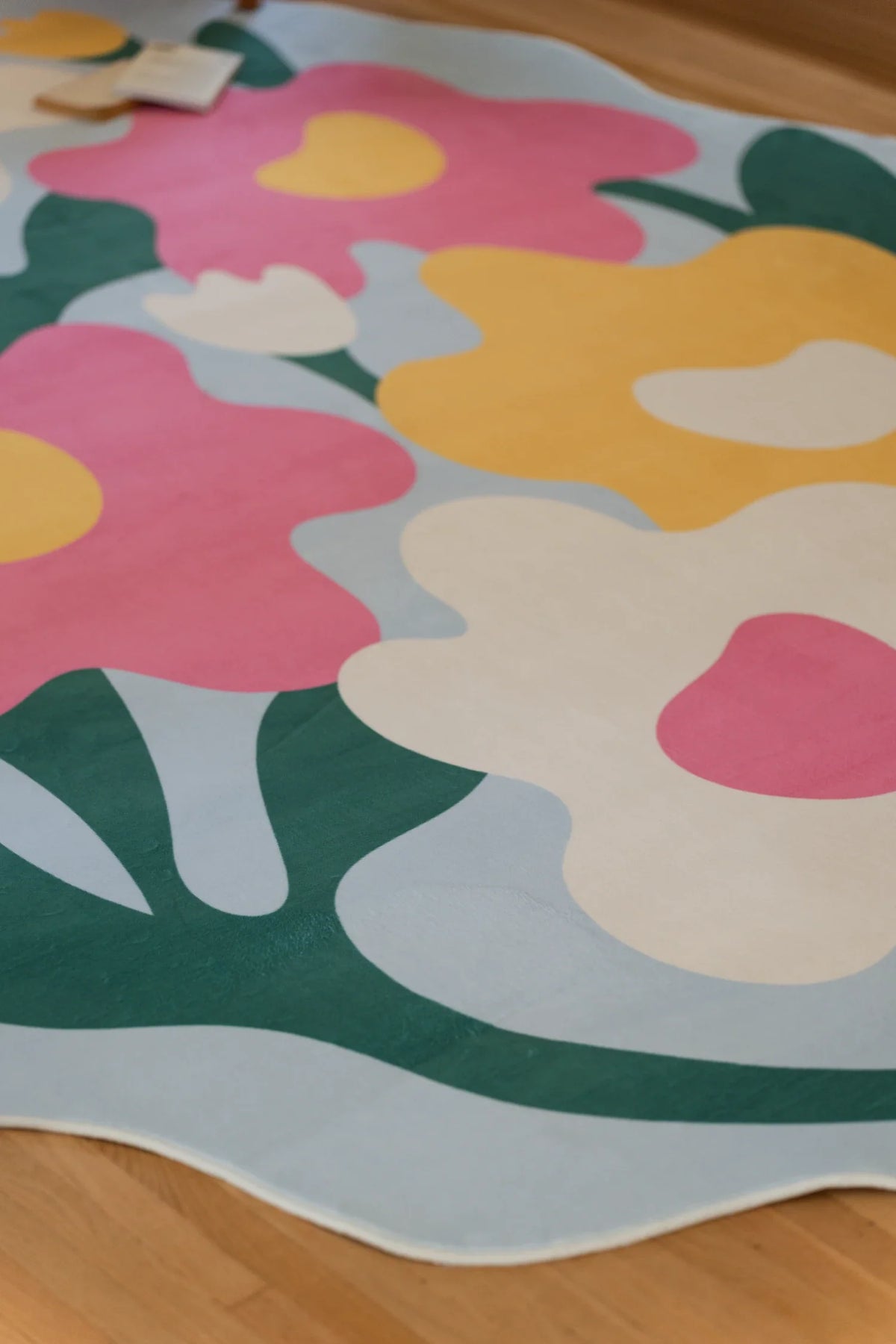 Partial close up of the irregular flower rug, showing pink, yellow, and white blooms connected by broad green stems