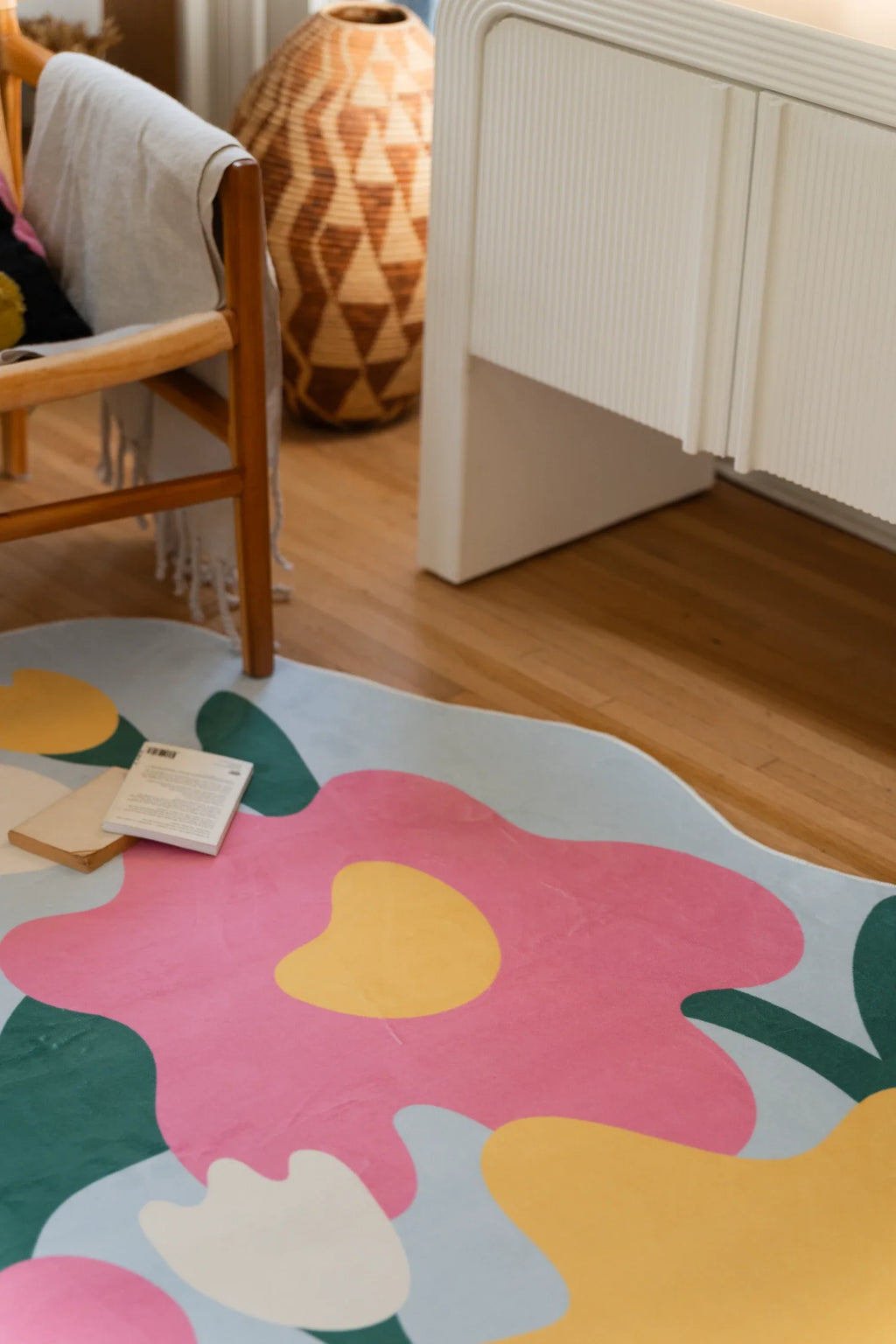 Corner crop of the floral area rug beside white cabinetry, with a pink flower, yellow bloom, and pale blue border
