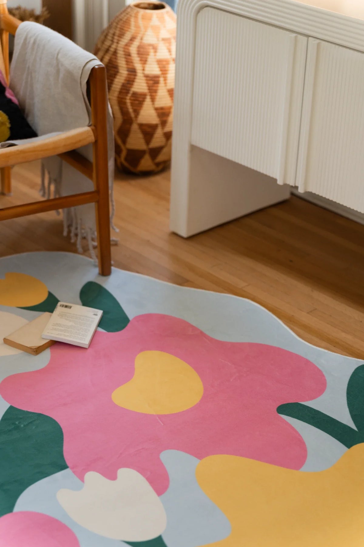 Corner crop of the floral area rug beside white cabinetry, with a pink flower, yellow bloom, and pale blue border