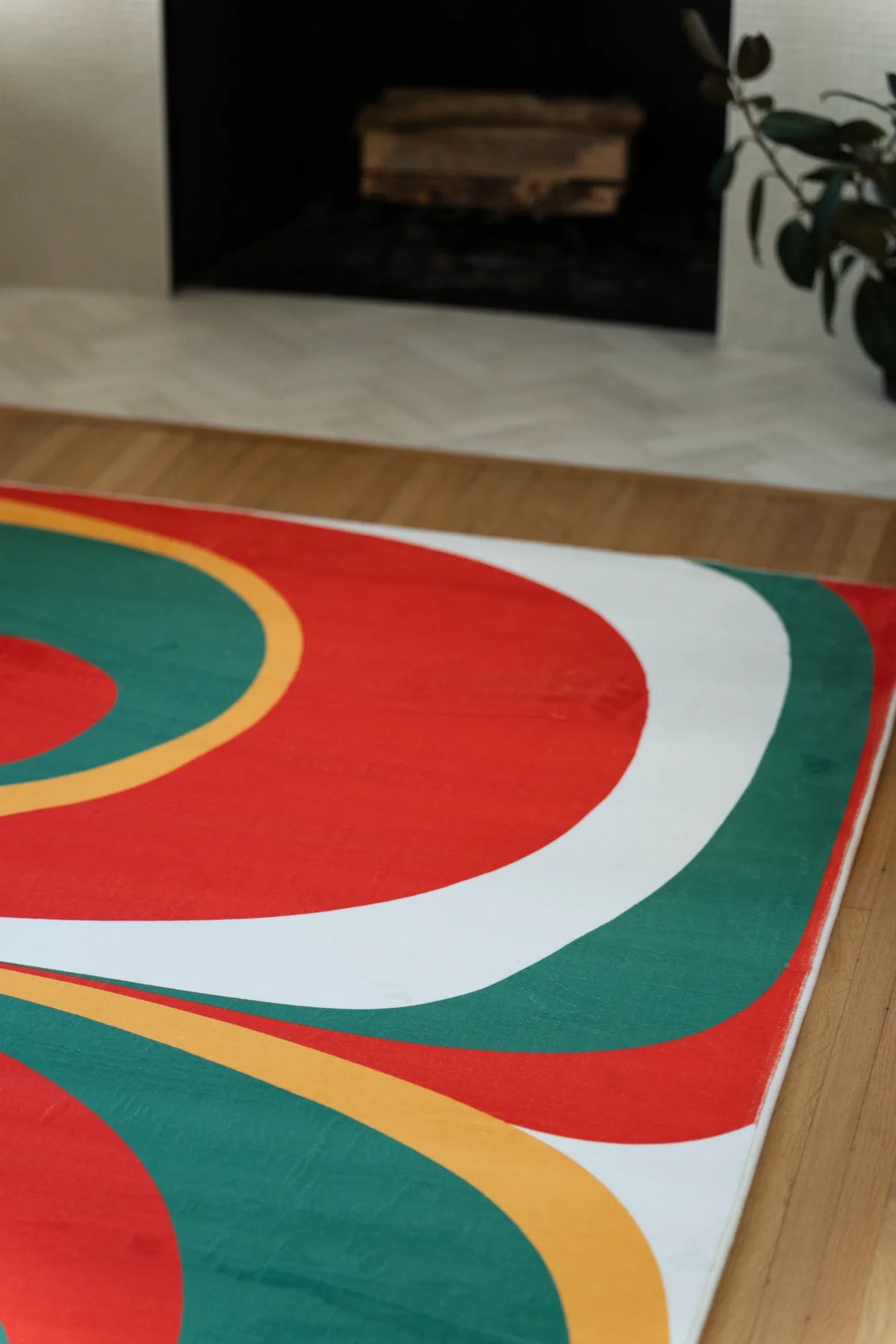 Partial view of the olive and red Tomato Twist rug near the fireplace, showing rounded red and green forms