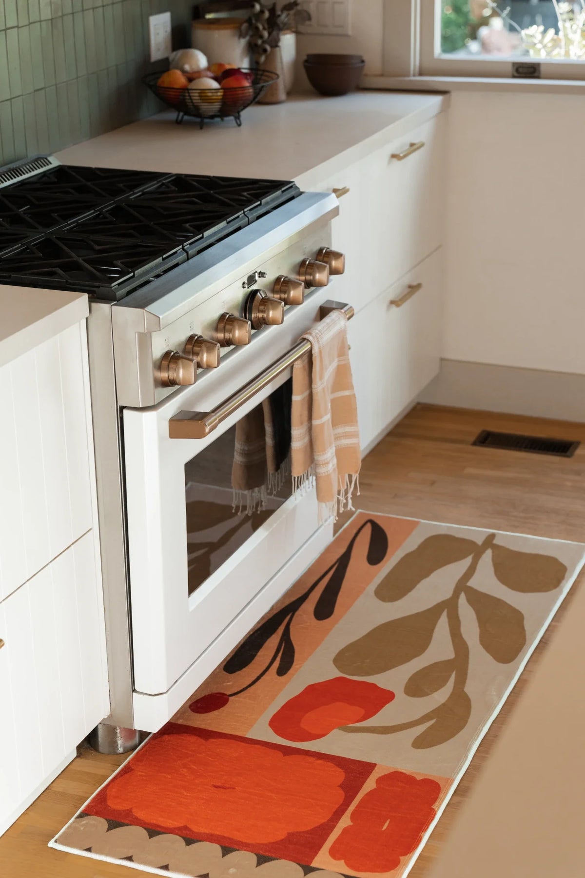 Rust red floral runner placed in front of a white oven, with bold patchwork panels and vine like shapes